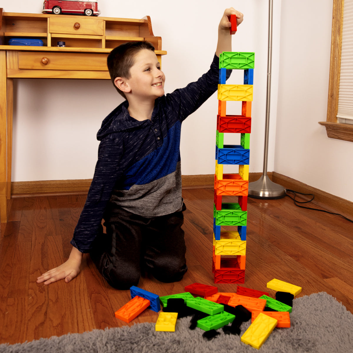 Blokix Creative Building Blocks from Atwood Toys, a boy stacking a tall tower of colorful red, orange, yellow, green, and blue interlocking blocks