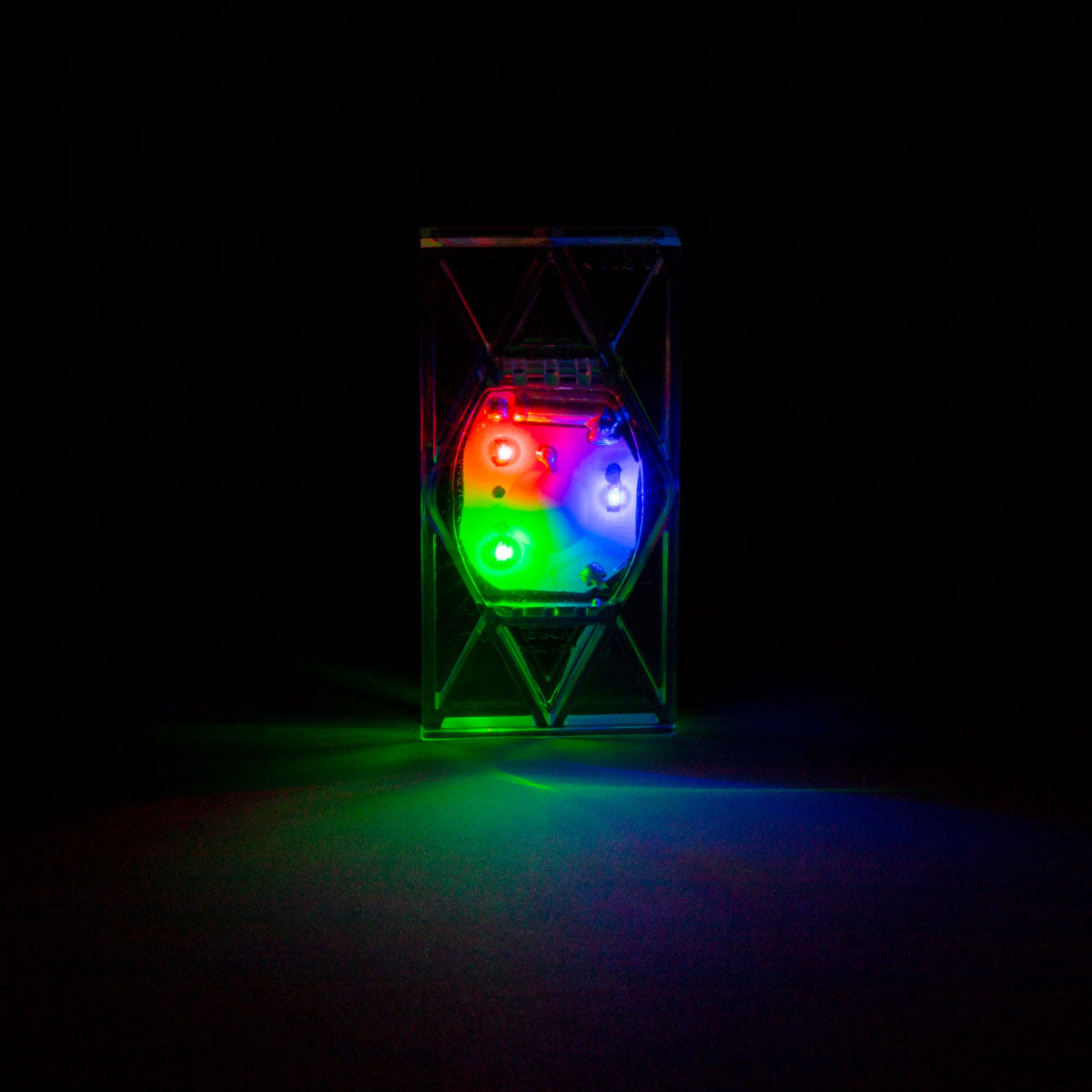A Light Up Electro Domino glowing red, green, and blue in a dark room, casting colorful light to show the LED brightness through the clear domino.