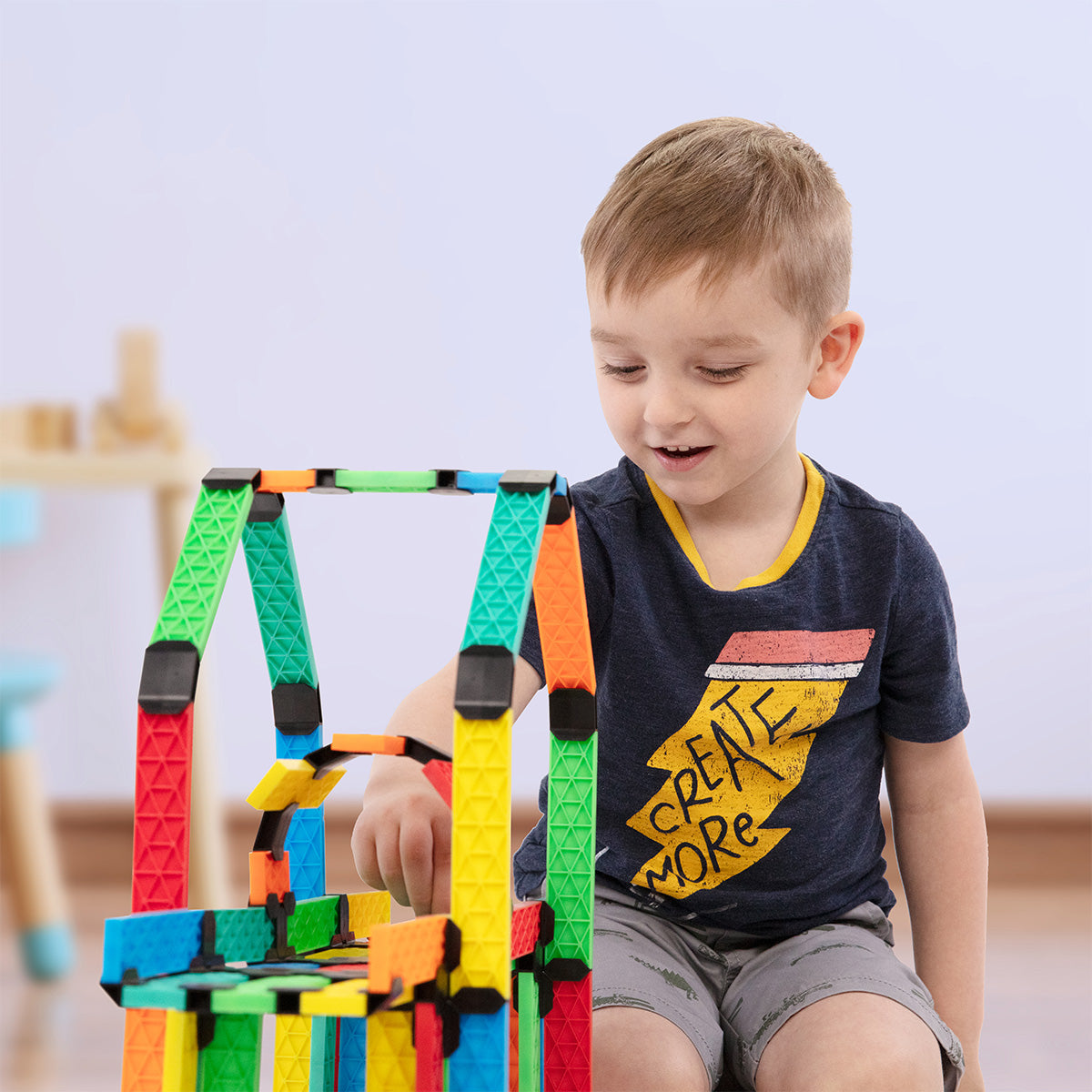 Atwood Toys Constructix Creative Explorer building set being used by a young boy to construct a colorful tower with green, red, yellow, blue, and orange clips and planks