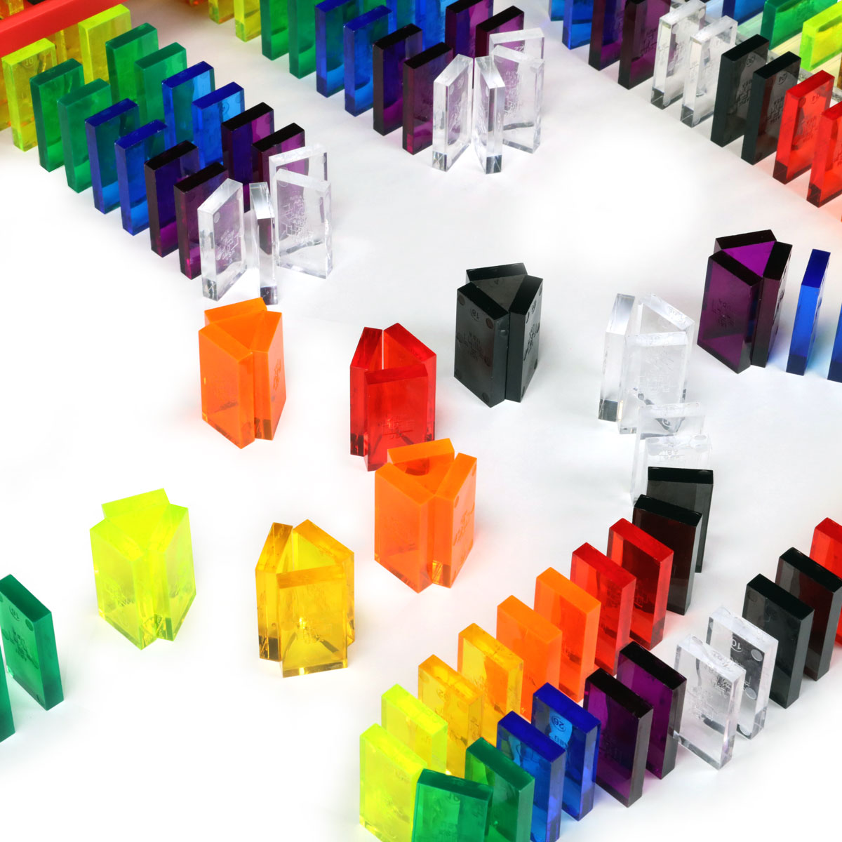 Bulk Dominoes Artisan Kit close-up of individual clear translucent Pro Dominoes in assorted colors including orange, red, yellow, green, blue, purple, clear, and black standing on white surface