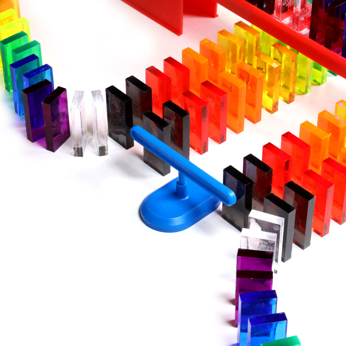 Bulk Dominoes Artisan Kit close-up of blue domino spinner accessory surrounded by clear translucent Pro Dominoes in rainbow colors mid-chain reaction setup