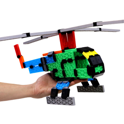 Helicopter model built from Atwood Toys Constructix Creative Explorer pieces in green, blue, red, and yellow with rotating blades, held in a hand to show the size of the build
