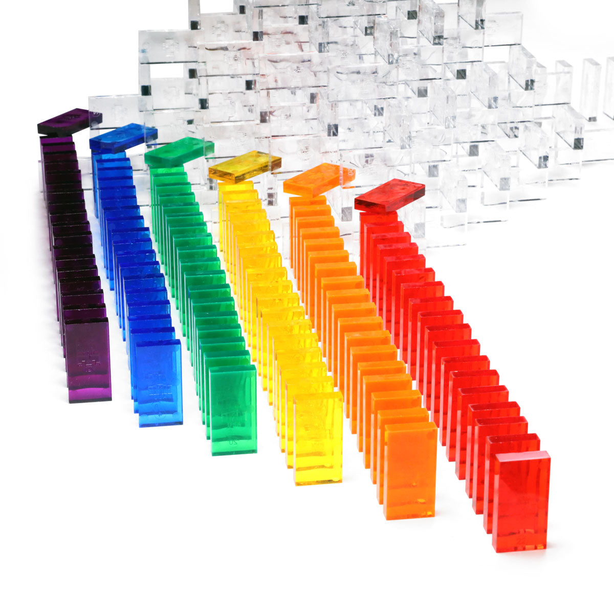 Bulk Dominoes Artisan Kit clear Pro Dominoes lined up in rainbow gradient from purple to red with clear domino 3D wall structure in the background