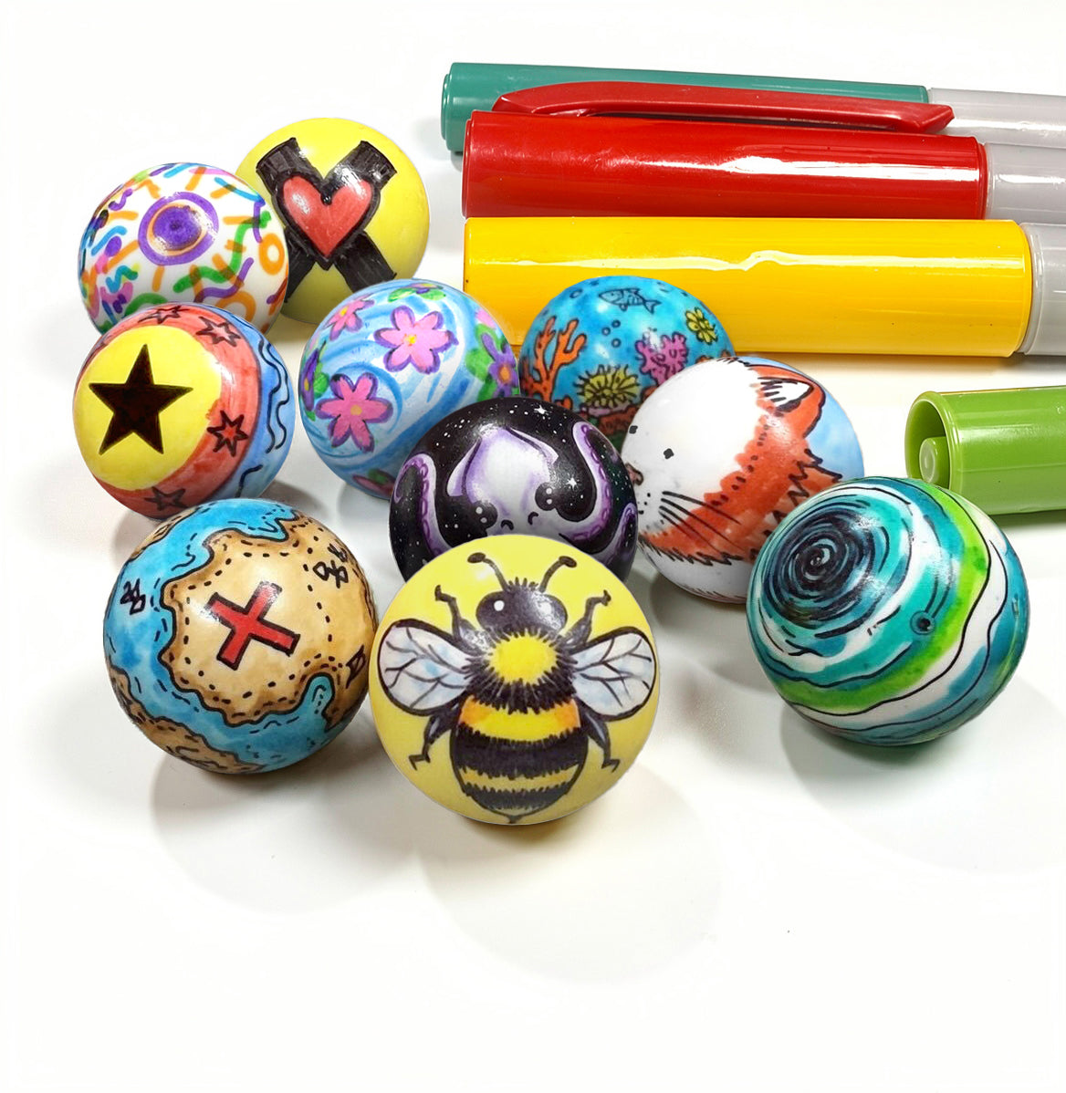 Pile of colorfully decorated Impact Marble Racing DIY marbles with markers, showing custom designs like a bee, star, cat, and galaxy.