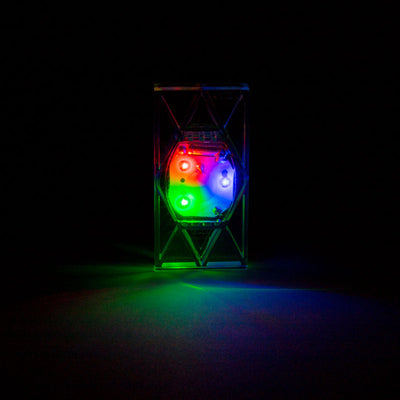 A Light Up Electro Domino glowing red, green, and blue in a dark room, casting colorful light to show the LED brightness through the clear domino.