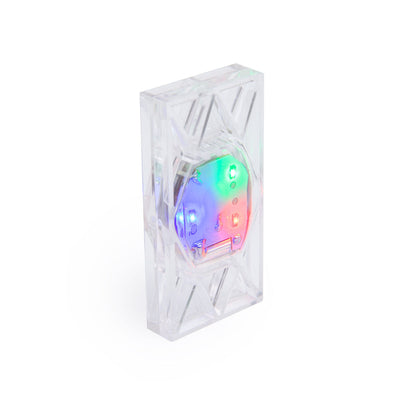 Close-up of a single clear Light Up Electro Domino from Atwood Toys, its internal RGB LED glowing red, green, blue, and purple through the crystal-cut tile.