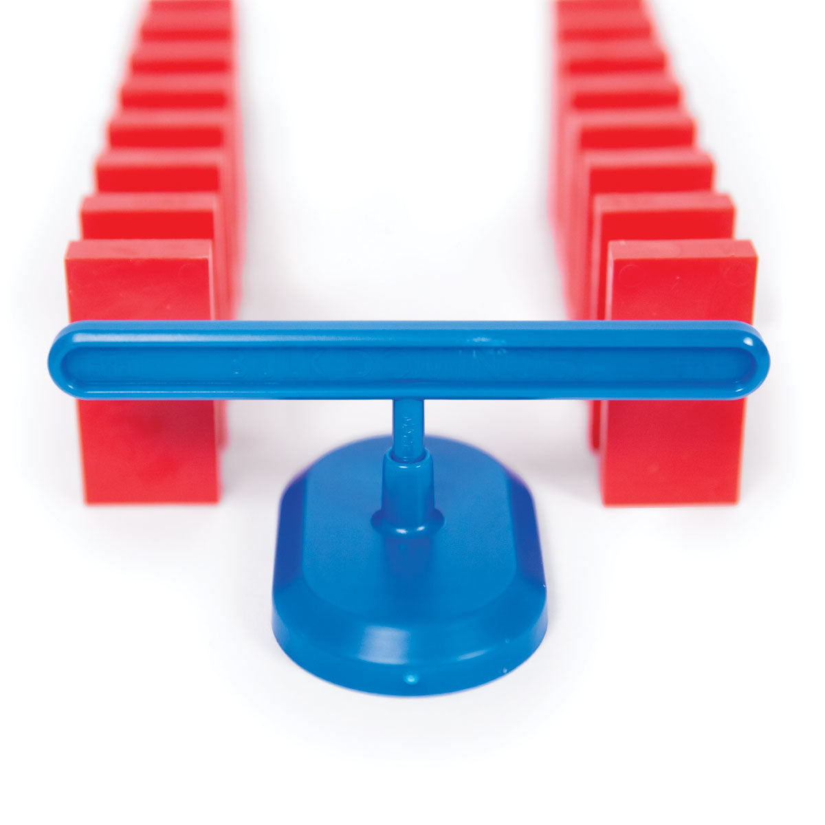 Atwood Toys Bulk Dominoes blue Domino Spinner positioned between two parallel rows of red toppling dominoes for direction changes in domino chain reactions