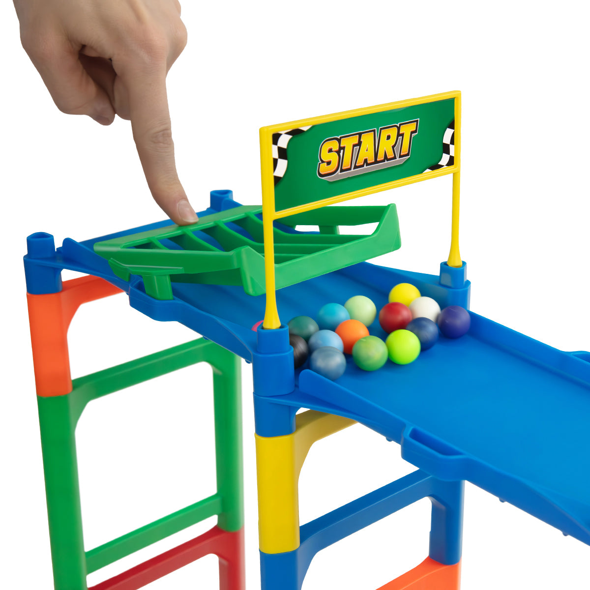 IMR Grand Prix Overdrive starting block close-up with hand pressing green release gate, START banner with checkered flags overhead, and colorful marbles loaded on blue track ready to race