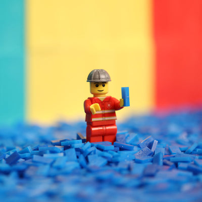 Atwood Toys World Record Mini Micro Dominoes size comparison with a LEGO minifigure standing on a pile of blue micro dominoes for visual scale reference