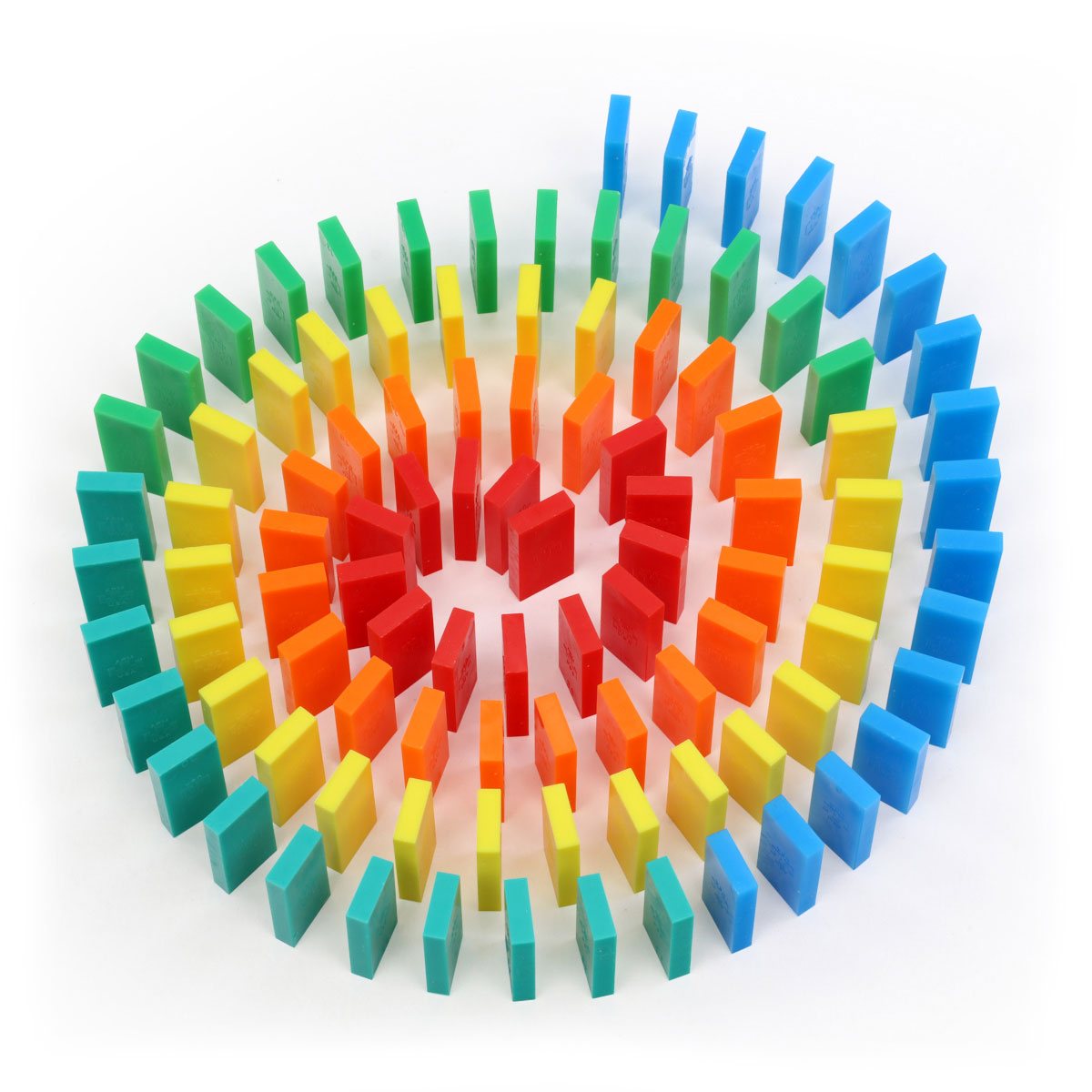 Rainbow spiral pattern built from Bulk Dominoes Mini Dominoes featuring red, orange, yellow, green, teal, and blue pieces arranged in concentric circles with vertical and horizontal placement.