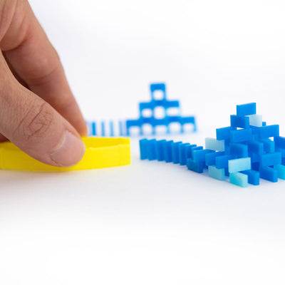 Atwood Toys World Record Mini Micro Dominoes scale shot showing a fingertip placing blue dominoes with the yellow setup tool, demonstrating the precision required for these tiny toppling dominoes