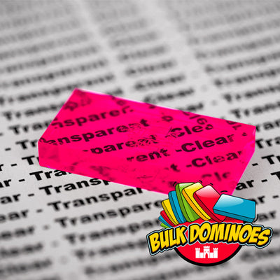Close-up of a single translucent Bulk Dominoes Clear Neon Pink Pro Domino held over printed text, showing the words clearly visible through the see-through neon pink tile.