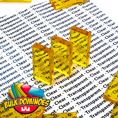 Close-up of a few translucent clear honey yellow Bulk Dominoes Clear Honey Pro Dominoes, showing the see-through golden tiles against a patterned background.