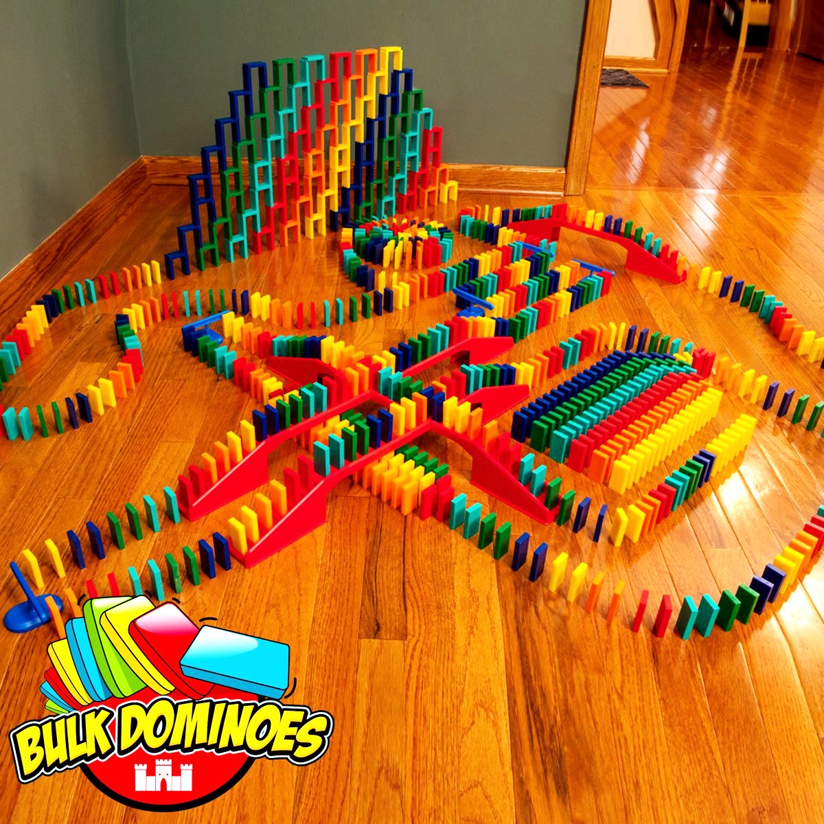 Bulk Dominoes Master Builder Kit setup on hardwood floor with colorful Pro Dominoes in chain reaction lines, red bridges, stacked domino walls, and blue spinners with Bulk Dominoes logo