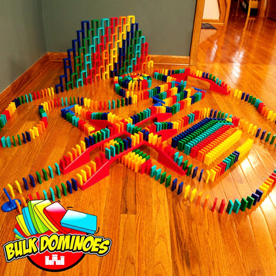 Bulk Dominoes Master Builder Kit setup on hardwood floor with colorful Pro Dominoes in chain reaction lines, red bridges, stacked domino walls, and blue spinners with Bulk Dominoes logo