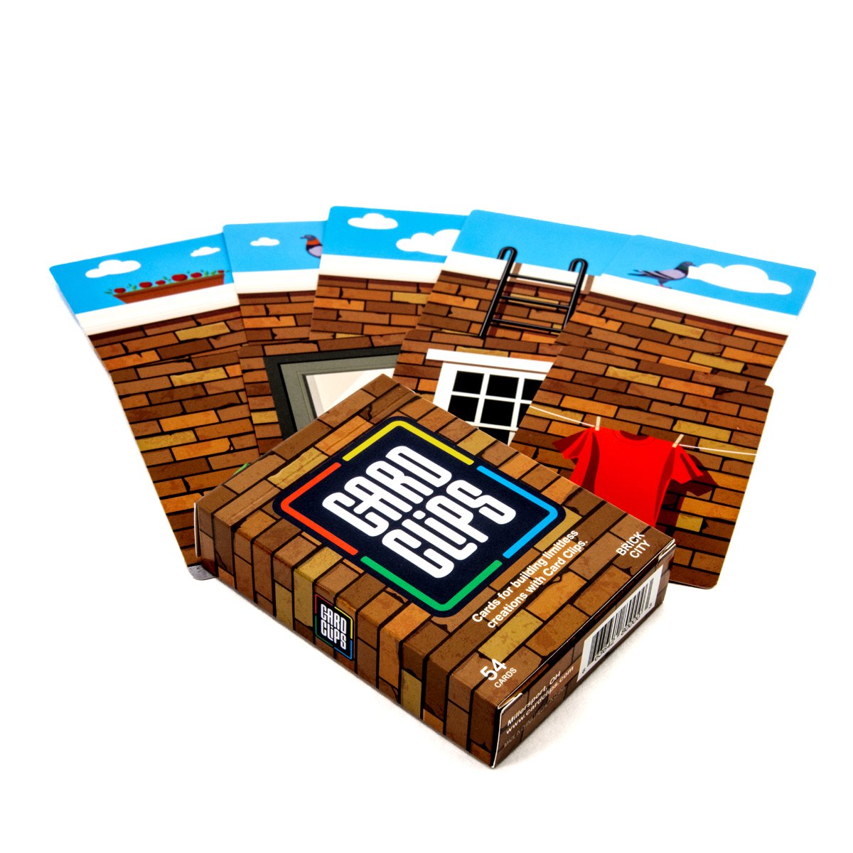 Building Cards Brick City deck from Atwood Toys, a fan of brick-wall and blue-sky building cards with windows, a clothesline, a planter, and a pigeon spread from the Card Clips deck box.