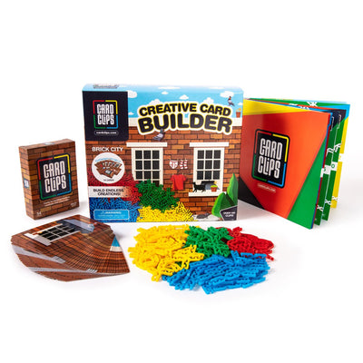 Creative Card Builder Brick City set from Atwood Toys, a retail box with a pile of yellow, green, red, and blue Card Clips, brick-printed building cards, and an instruction booklet for building towers, walls, and 3D structures.
